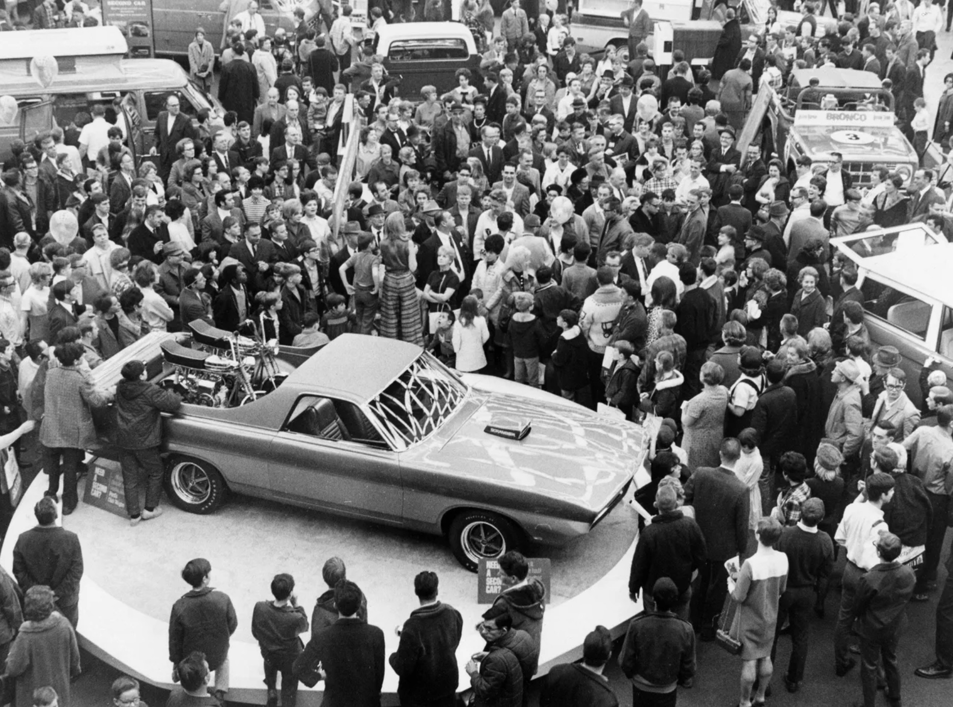 Large crowds surround a car at the Detroit Auto Show 